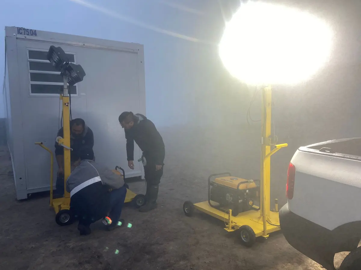 Equipe da Revlo ajustando duas torres de iluminação acesas na neblina, ao lado de um contêiner