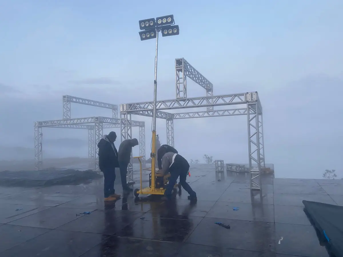 Torres de iluminação Revlo em operação ao lado de estrutura metálica de evento, sob neblina