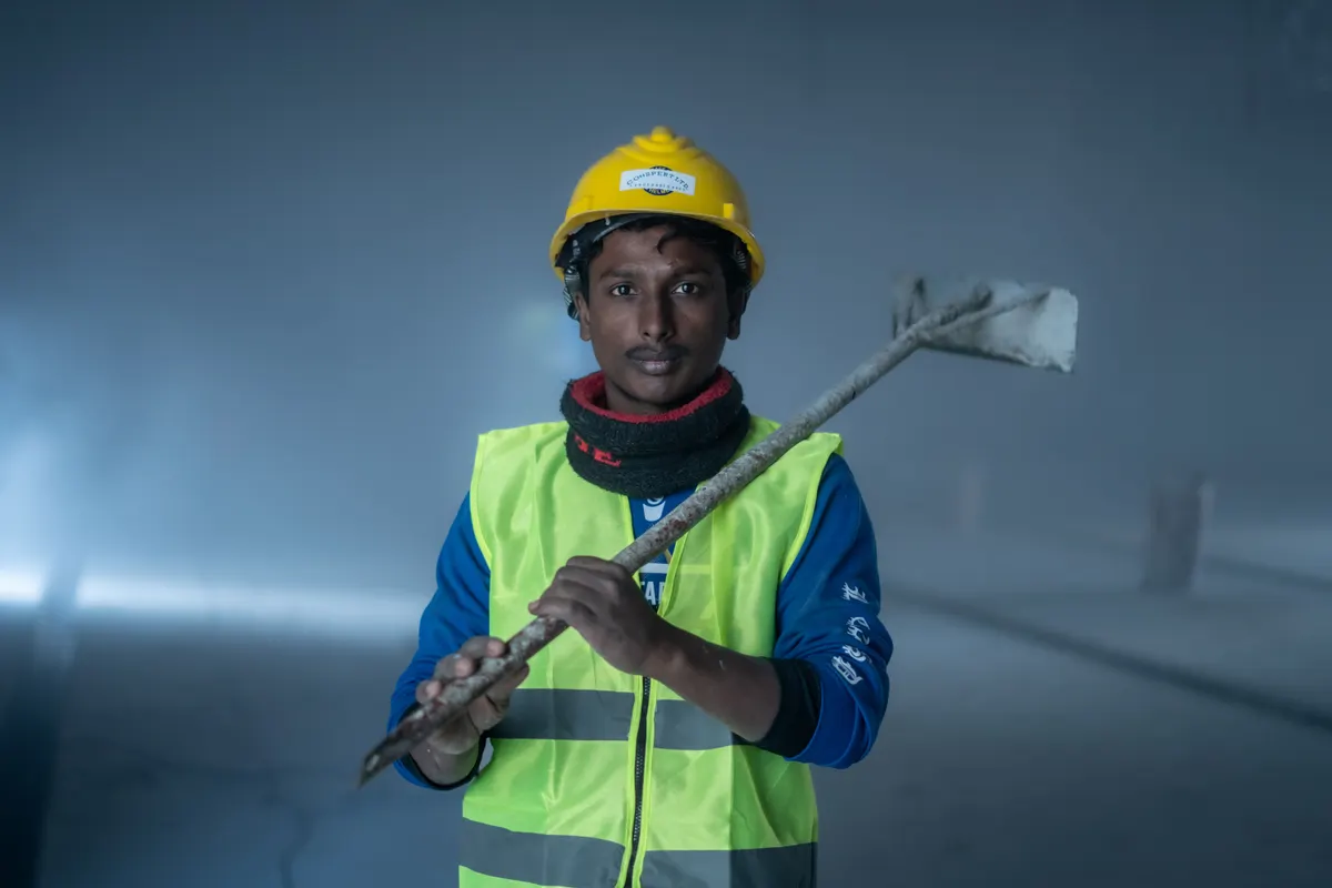 Retrato de operário de colete refletivo e capacete segurando ferramenta, iluminado por refletor