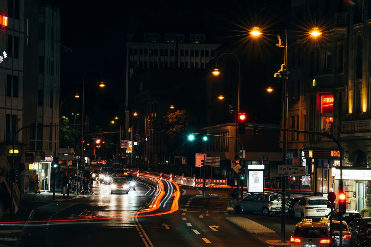 Rua urbana à noite com semáforos acesos e rastros de luz dos veículos