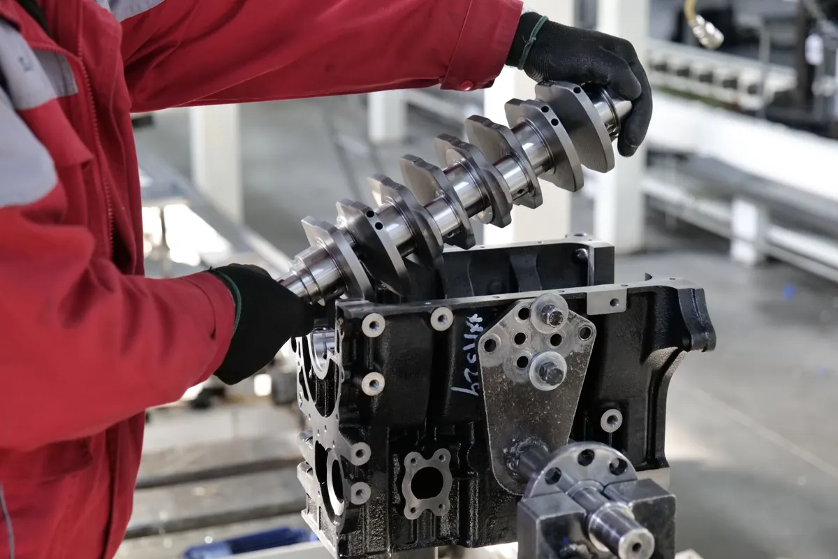 Técnico de uniforme manuseando bloco de motor em bancada industrial